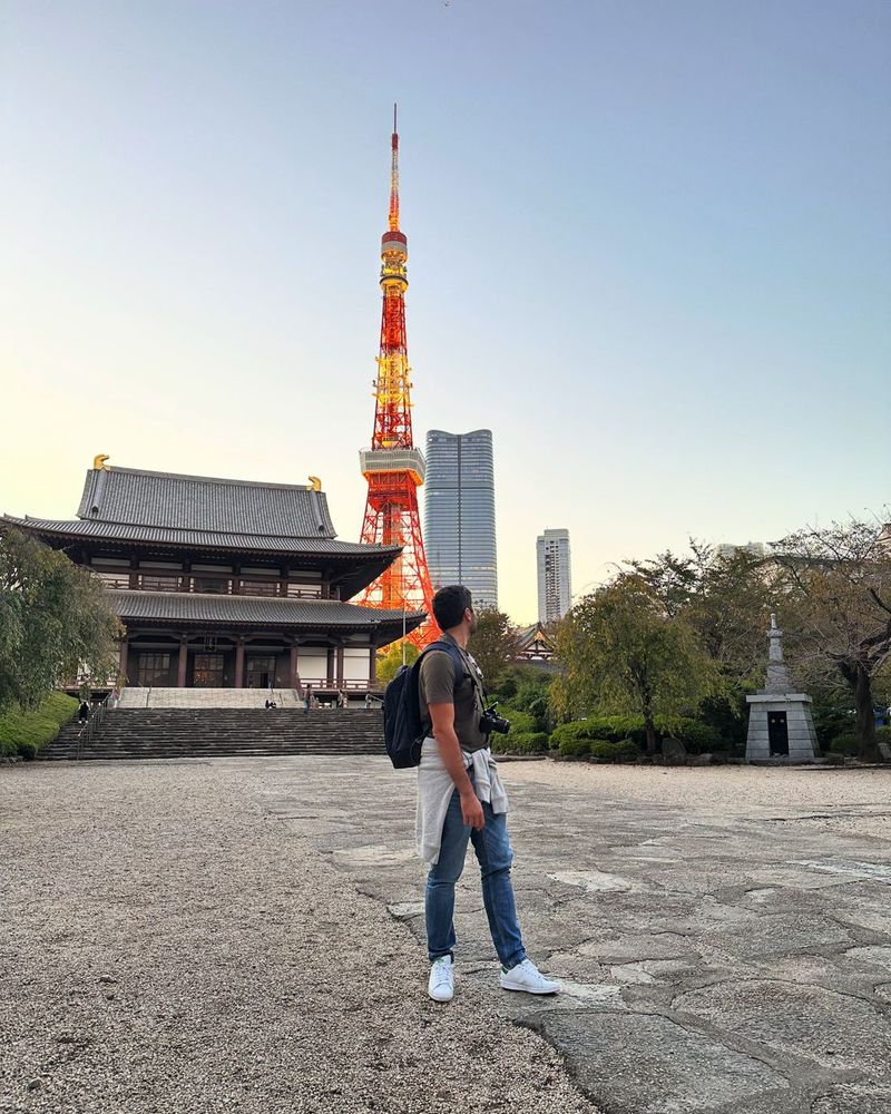 Oscar looking up at the illuminated Tokyo Tower beside Zojo-ji temple at dusk